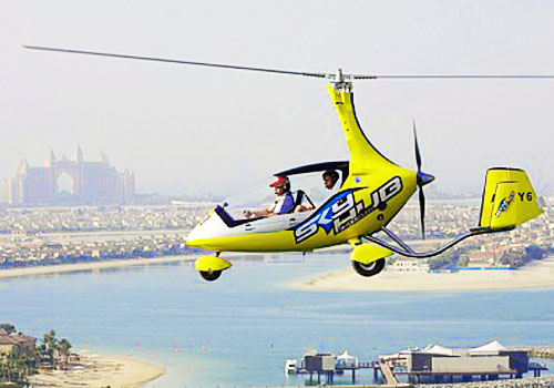 A yellow gyrocopter is flying above the sea in Dubai