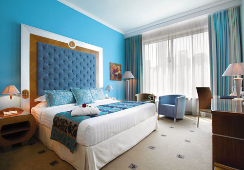 Kind bed in a hotel with light blue decor and big windows