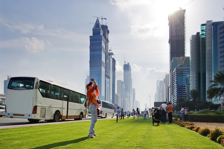 A woman is taking picture of tall buildings in front a tourist bus