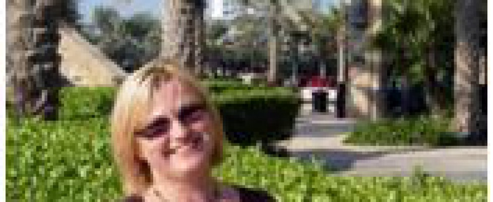 A woman is standing and smiling with palm trees in background