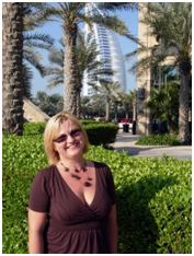 A woman is standing and smiling with palm trees in background