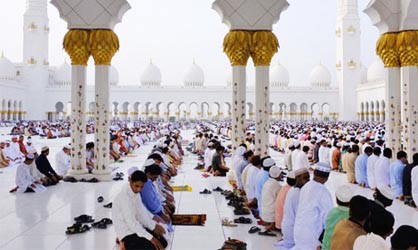 Men kneeling in rows praying in the white floors of Sheikh Zayed Mosque