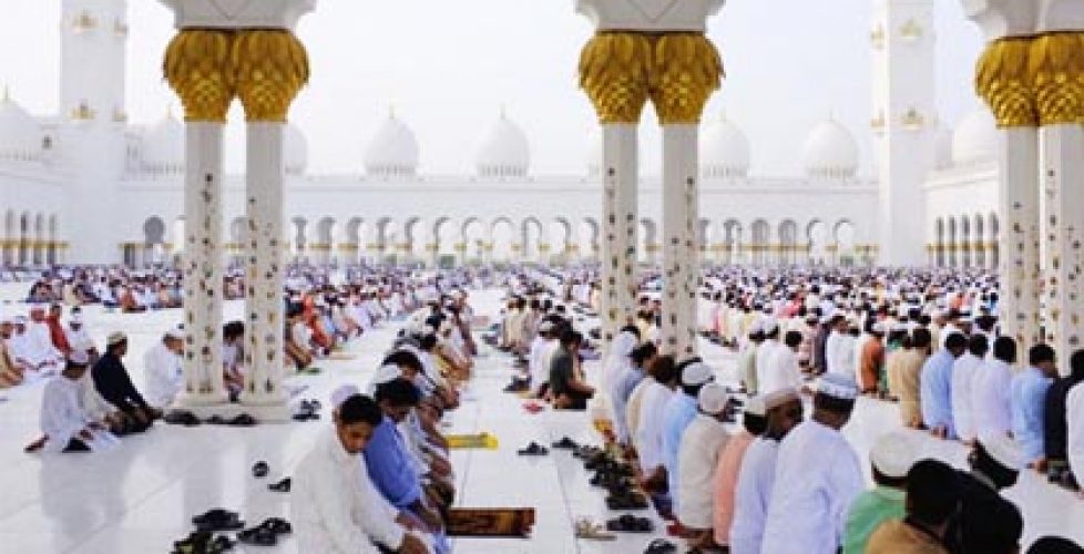 Men kneeling in rows praying in the white floors of Sheikh Zayed Mosque