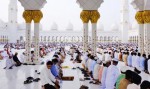 Men kneeling in rows praying in the white floors of Sheikh Zayed Mosque