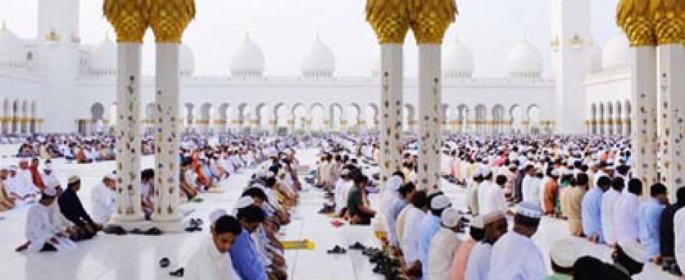 Men kneeling in rows praying in the white floors of Sheikh Zayed Mosque